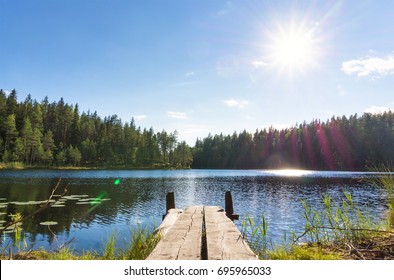 Traditional Finnish and Scandinavian view. Beautiful lake on a summer day and an old rustic wooden dock or pier in Finland. Sun shining on forest and woods in blue sky. - Powered by Shutterstock