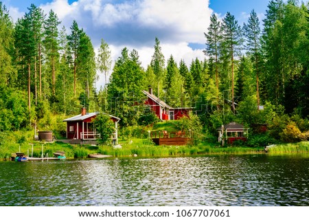 A traditional Finnish wooden cottage with a sauna and a barn on the lake shore. Summer landscape. Rural Finland.