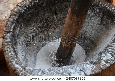 Traditional folk wisdom tribe karen people use large wooden mortar and big wood pestle for pounding rice grains thoroughly to powder for cooking local food at Baan Taphoen Khi in Suphanburi, Thailand
