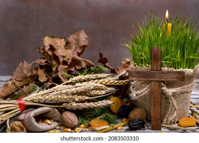 Traditional food for orthodox Christmas eve. Yule log or badnjak, cereals, dried fruit, wooden cross and a burning candle in green wheat on a wooden table. Concept celebration orthodox Christmas.
