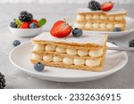 Traditional French dessert millefeuille with vanilla cream and fresh berries on a white plate on a gray concrete background