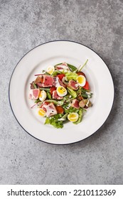 Traditional French Nicoise Salad With Grilled Tuna, Quail Eggs, Potatoes, Green Beans, Capers And Tomatoes Over Gray Concrete Background. Overhead View, Copy Space