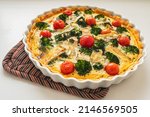 Traditional french pie. Quiche Loraine with mushrooms, broccoli, tomatoes and cheese. top view, in ceramic baking dish on heat-resistant stand