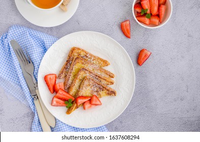 Traditional French toast sprinkled with powdered sugar with fresh strawberries on a white plate with a cup of tea. Delicious breakfast. Horizontal orientation. Top view, copy space.