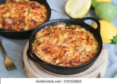 A traditional French zucchini gratin with browned crust grilled grate cheese in a baking black casserole, with variety colorful zucchini fruits in background - Shutterstock ID 1761536825