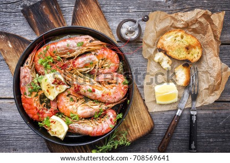 Traditional fried black tiger prawn with garlic bread as top view in a black frying pan 