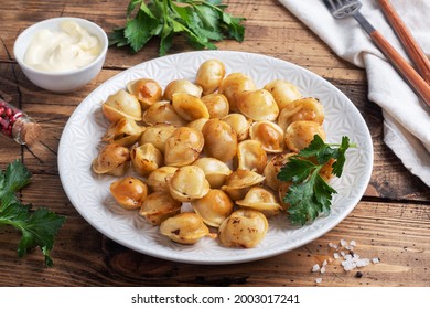 Traditional fried pelmeni, ravioli, dumplings filled with meat on plate, russian kitchen. Wooden rustic table, copy space