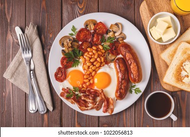 Traditional full English breakfast with fried eggs, sausages, beans, mushrooms, grilled tomatoes and bacon on wooden background. Top view - Shutterstock ID 1022056813