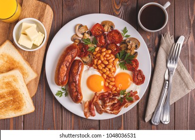 Traditional full English breakfast with fried eggs, sausages, beans, mushrooms, grilled tomatoes and bacon on wooden background. Top view