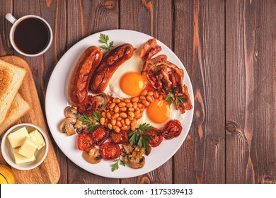 Traditional full English breakfast with fried eggs, sausages, beans, mushrooms, grilled tomatoes and bacon on wooden background. Top view - Shutterstock ID 1175339413