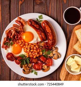 Traditional full English breakfast with fried eggs, sausages, beans, mushrooms, grilled tomatoes and bacon on wooden background. Top view - Shutterstock ID 725440849
