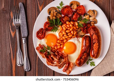 Traditional full English breakfast with fried eggs, sausages, beans, mushrooms, grilled tomatoes and bacon on wooden background. Top view - Shutterstock ID 753406096