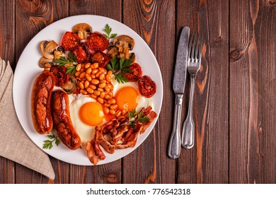 Traditional full English breakfast with fried eggs, sausages, beans, mushrooms, grilled tomatoes and bacon on wooden background. Top view - Shutterstock ID 776542318