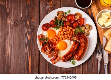 Traditional full English breakfast with fried eggs, sausages, beans, mushrooms, grilled tomatoes and bacon on wooden background. Top view - Shutterstock ID 776542498
