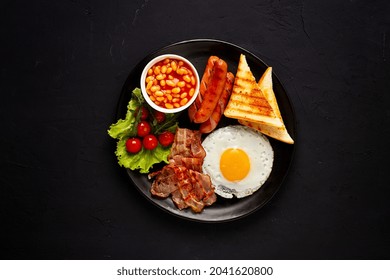 Traditional Full English Breakfast, On A Black Background, Fried Eggs With Fried Bacon, Sausages, White Beans ,cherry Tomatoes, Horizontal, No People,