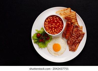 Traditional Full English Breakfast, On A Black Background, Fried Eggs With Fried Bacon, Sausages, White Beans ,cherry Tomatoes, Horizontal, No People,