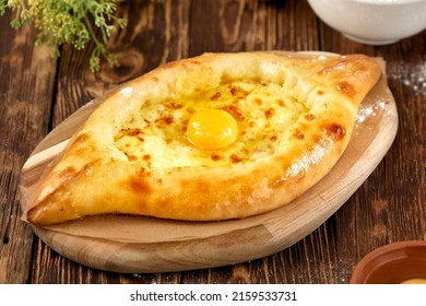 Traditional georgian pastry - adjarian khachapuri with cheese and raw yolk. Khachapuri with egg on wooden background in rustic style. Adjara khachapuri with ingredients. Georgian cuisine