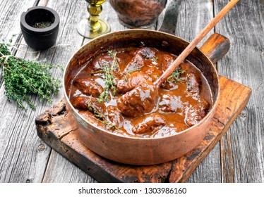 Traditional German braised pork cheeks in brown red wine sauce with mushroom and onions as closeup in a casserole