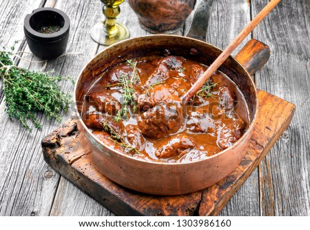 Traditional German braised pork cheeks in brown red wine sauce with mushroom and onions as closeup in a casserole