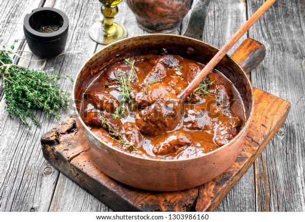 Traditional German\
braised pork cheeks in brown red wine sauce with mushroom and\
onions as closeup in a\
casserole