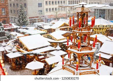 Traditional German Christmas Market In The Historic Center Of A City In Germany During Snow. Stands, Traditional Pyramid With Candles On Winter Day
