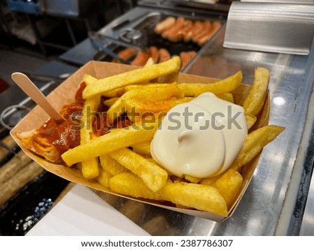 Traditional german currywurst with tomato sauce, curry powder and french fries in a paper plate in the female hand close up