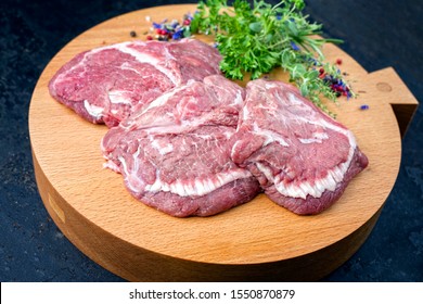 Traditional German raw beef cheeks offered as closeup with herb and spice on a modern design wooden cutting board