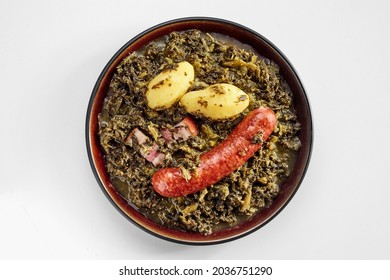 Traditional German Spicy Sausage With Fresh Boiled Or Braised Kale And Two Baby Potatoes In An Overhead View On An Earthenware Plate Isolated On White