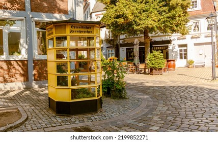 Traditional German telephone box with flowers. Old yellow telephone booth in Germany with text öffentlicher fernsprecher - public telephone
