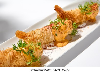 Traditional greek appetizer - kataifi wrapped shrimps on white plate. Crispy shrimp in kataifi crust in summer day. Shrimp appetizer fried in kataifi dough. Crispy prawns in modern style