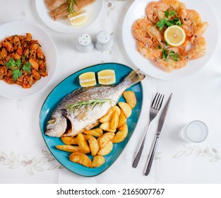 Traditional  Greek food, Dorada fish with Greek salad, Mediterranean traditional menu, Grilled sea bream, shrimps or prawns  zucchini, variety of seafood, mussels, tzatziki, potatoes, feta and ouzo - Shutterstock ID 2165007767