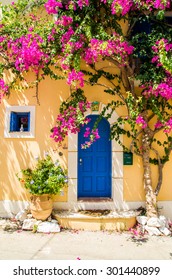 Traditional greek house with flowers in Assos, Kefalonia island, Greece. Blue door and blue window surrounded by magenta flowers.