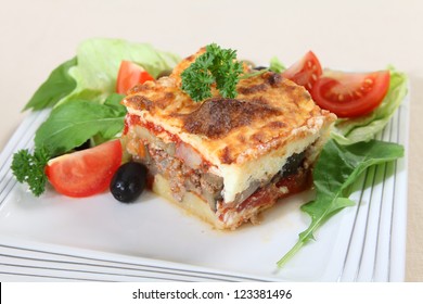 A Traditional Greek Moussaka, Made With Layers Of Potato, Aubergine, Meat, And Tomato Sauce, Topped With Bechamel Sauce And Served With Salad.