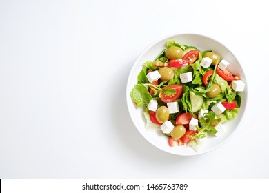 Traditional greek salad with fresh ingredients, feta cheese, olives, red tomatoes, cucumbers and greens in ceramic bowl, isolated on white background. Top view, close up, copy space. - Powered by Shutterstock