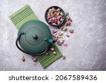 Traditional green or turquoise asian cast iron kettle with herbal tea of dried rose buds on grey concrete background