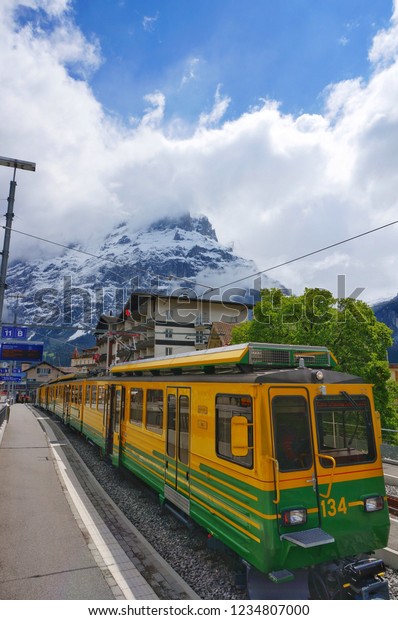 Traditional green and yellow train in\
Grindelwald First with snow mountain backgrounds\
view