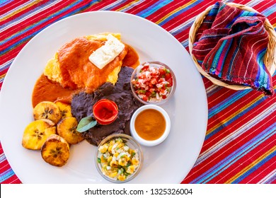 Traditional Guatemalan breakfast of eggs, black beans, cheese & fried plantain with tortillas wrapped in basket on handwoven Maya textile tablecloth in restaurant at Lake Atitlan