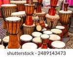 Traditional handmade djembe drums displayed at a market. The single-headed goblet drum comes from West Africa. Its body is made from a hollowed-out tree trunk.