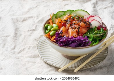 Traditional Hawaiian Poke bowl with salmon, red cabbage, wakame, carrot, cucumber, pomegranate, edamame, black list, watercress and nori on a gray background