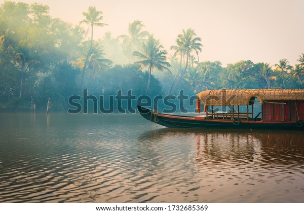 A traditional house boat is anchored on the shores\
of a fishing lake in the palm tree jungle at sunset, in the\
Backwaters, a popular destination for yoga retreats and nature\
lovers in Kerala, India