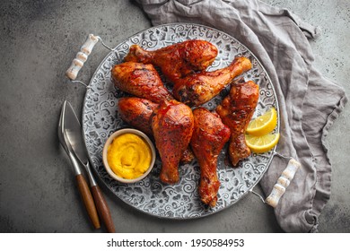 Traditional Indian dish Tandoori chicken legs served with exotic yellow sauce and lemon wedges on rustic aluminum plate on grey concrete background from above 
