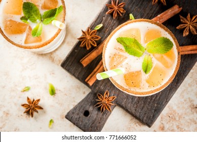 Traditional Indian Drink Is Iced Tea Or Chai Masala, With Ice Cubes From Chai, Milk And Mint Leaves. With Striped Straws, On A Wooden Board. On Light Beige Stone Table. Copy Space Top View