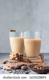 Traditional Indian drink - masala chai tea (milk tea) with spices in drinking glasses on grey stone background with spices for making tea.