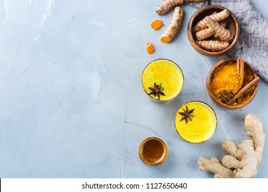 Traditional indian drink turmeric golden milk in a glass with ingredients, ginger, curcuma, honey on a kitchen table. Top view flat lay copy space background