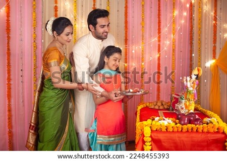 Traditional Indian family worshiping Lord Krishna on Krishna Janmashtami - Festival concept. Stock image of a happy family holding a puja thali together and doing aarti - Hindu culture, spiritual f...
