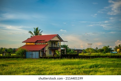 Traditional Indian village house surrounded by green grass and beatiful cloudy blue sky. Village landscape.