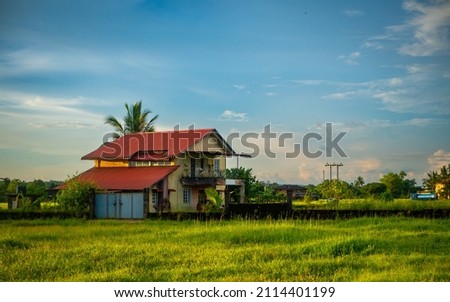 Traditional Indian village house surrounded by green grass and beatiful cloudy blue sky. Village landscape.