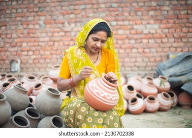Traditional Indian woman potter artist painting and decorating design on clay pot for sale, handicraft, skill india.