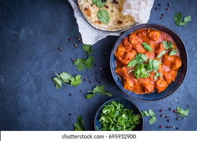 Traditional Indian/British dish chicken tikka masala background. Spicy chicken tikka masala/curry in bowl, indian bread naan, fresh cilantro. Indian style dinner. Space for text. Top view. Indian food
