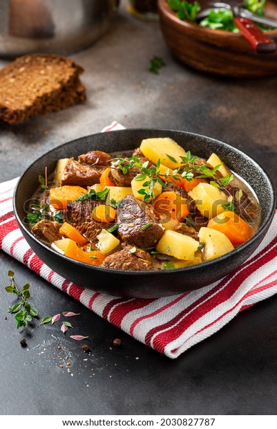 Traditional Irish stew in a black bowl on\
a dark background. Stew of lamb, potatoes, onions, carrots, and\
thyme. Traditional dish of St. Patrick\'s\
Day.